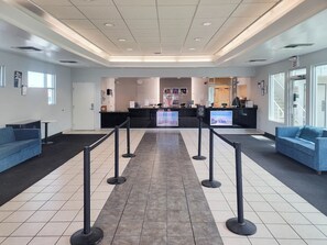 A reception area with a check-in counter, two blue sofas, a black barrier, and a tiled floor. - Studio 6 Suites Las Vegas, NV – Tropicana (Las Vegas)