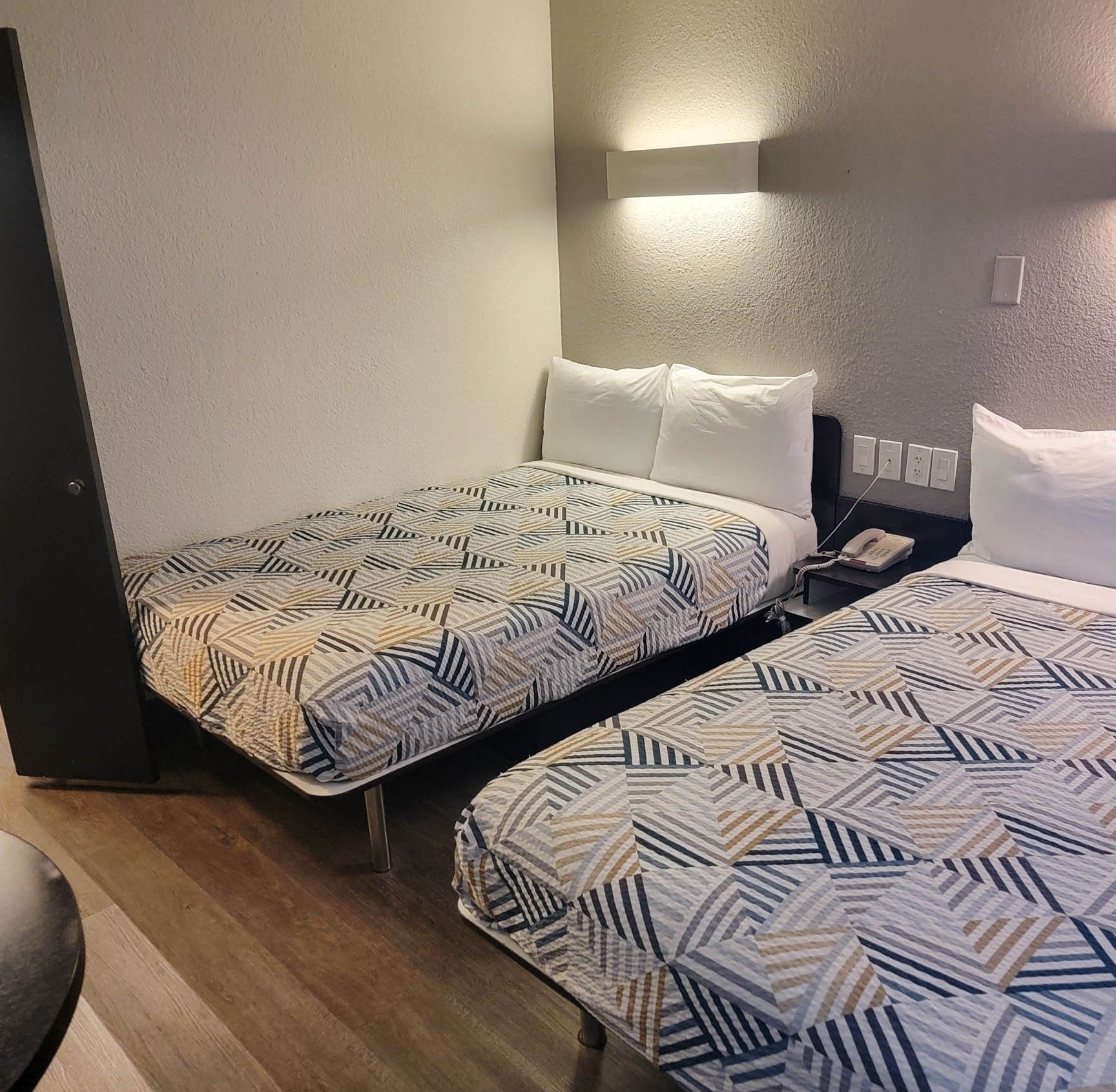 Een hotelkamer met twee bedden, elk voorzien van beddengoed met een patroon, een nachtkastje, een lamp en een telefoon.