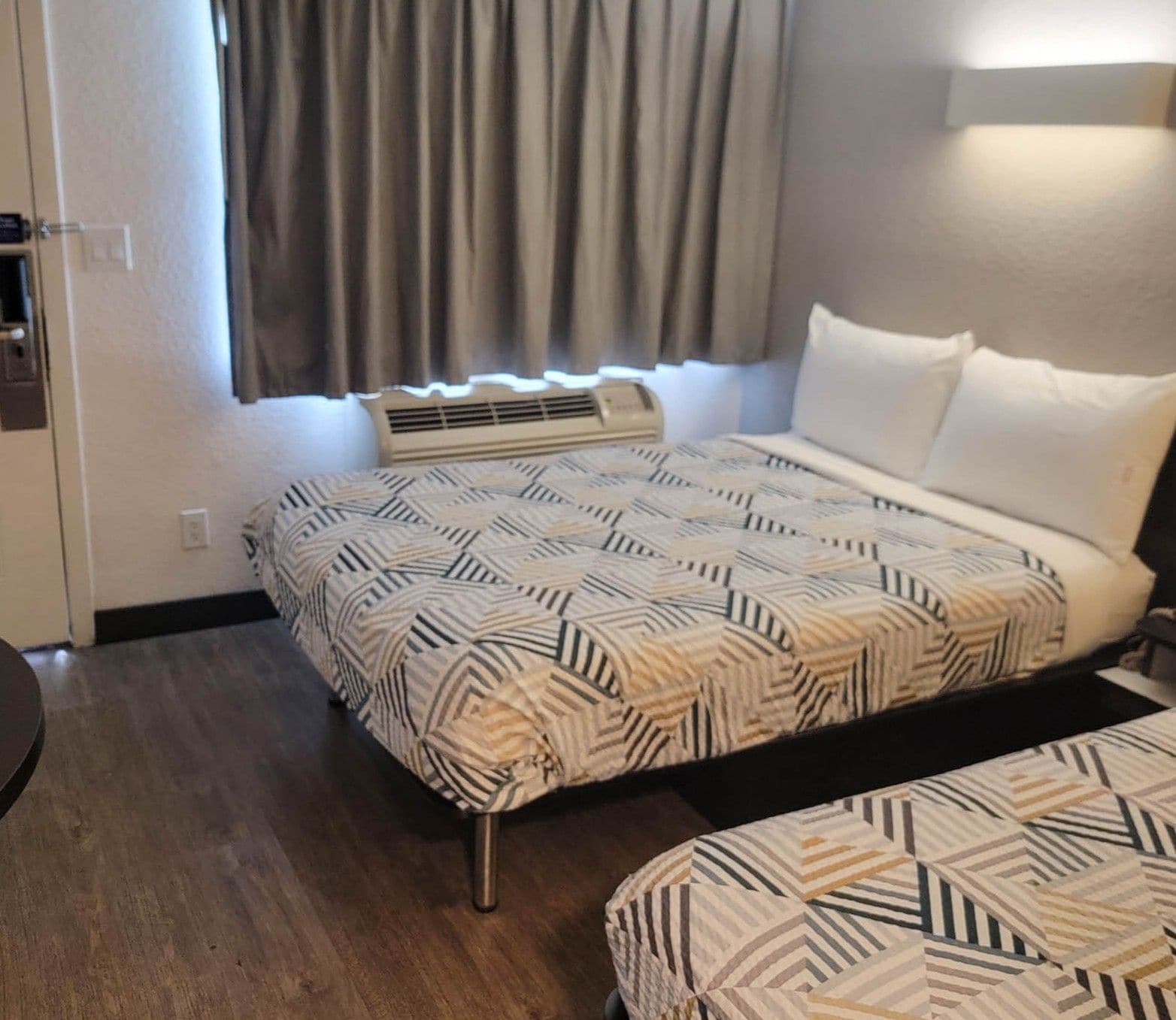 Een hotelkamer met een bed, nachtkastje, raam met gordijnen en een wandairconditioner.