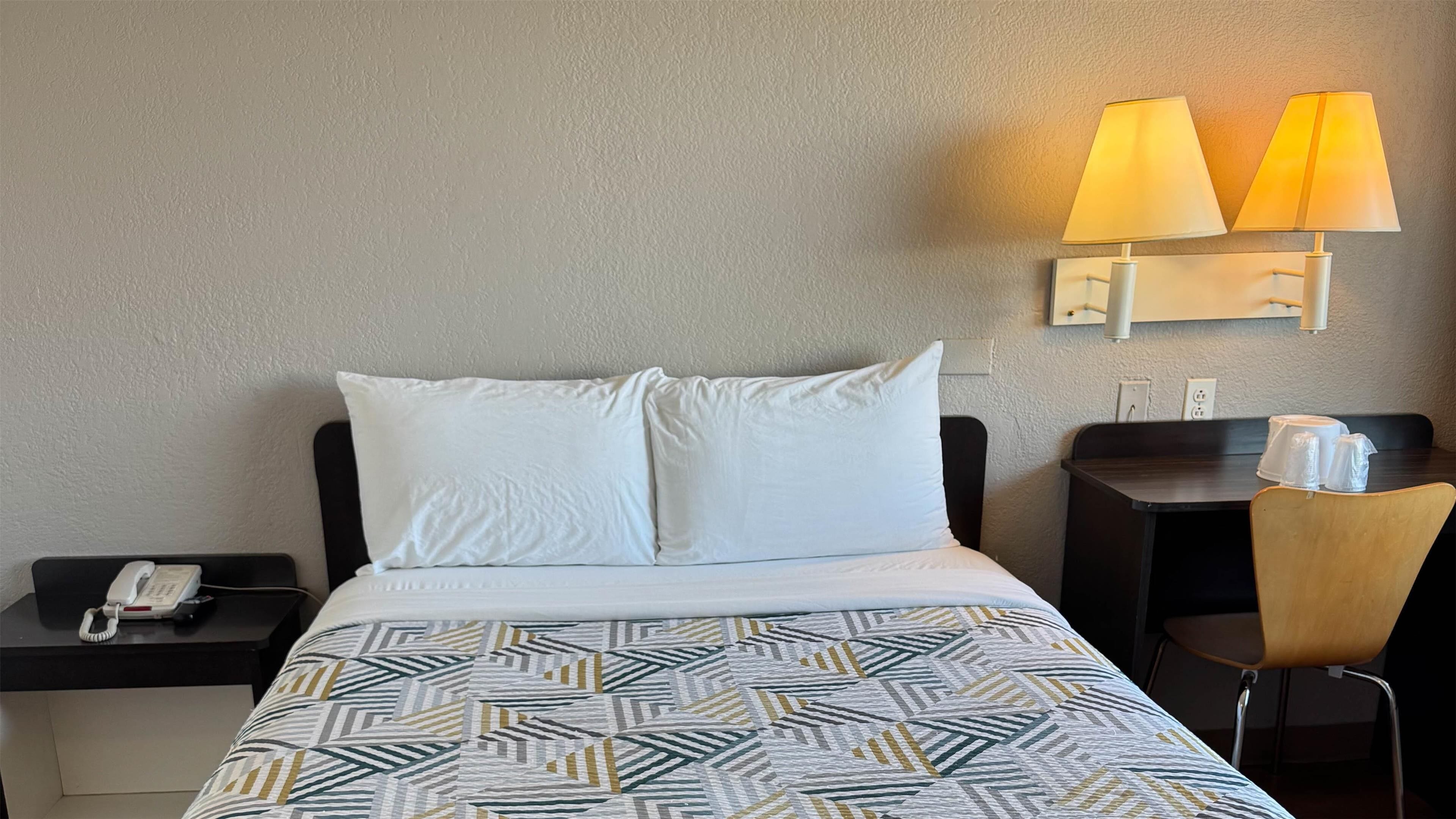 Een hotelkamer met een bed, twee bedlampen, een telefoon, een stoel en een kleine tafel met een lamp.