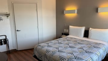 A hotel room with a bed, a desk, and a chair. There is a door, a wall-mounted light, and a phone on the nightstand.