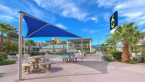 An outdoor pool area with tables and chairs, a covered seating area, and a sign indicating a collection point. - Studio 6 Suites Las Vegas, NV – Tropicana (Las Vegas)
