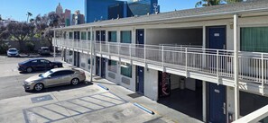 A motel with a covered parking area, multiple rooms, and a city skyline in the background. - Studio 6 Suites Las Vegas, NV – Tropicana (Las Vegas)