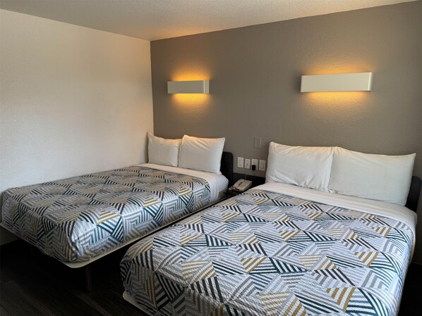 A hotel room with two beds, each with patterned bedding, a bedside table with a phone, and wall-mounted lighting.