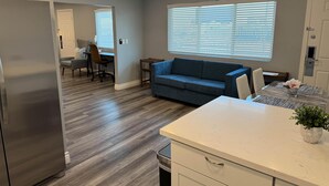 A modern kitchen with a built-in refrigerator, a dining area with a table and chairs, a blue sofa, and a ceiling fan. - Studio 6 Suites Las Vegas, NV – Tropicana (Las Vegas)