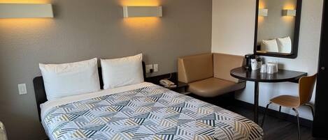 Una habitación de hotel con una cama, un escritorio, una silla y un espejo.