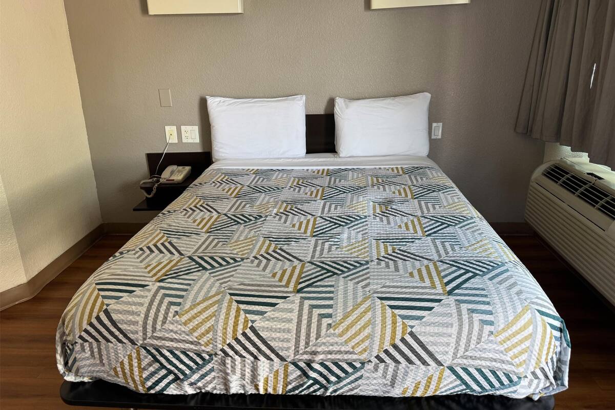 A hotel room with a bed, two bedside tables, a telephone, and a wall-mounted air conditioner.