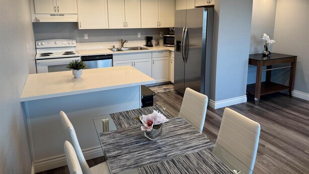 A modern kitchen with white cabinets, a stainless steel refrigerator, and a dining area with a table and chairs. - Studio 6 Suites Las Vegas, NV – Tropicana (Las Vegas)
