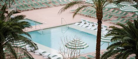 A pool area with lounge chairs and umbrellas, surrounded by palm trees.