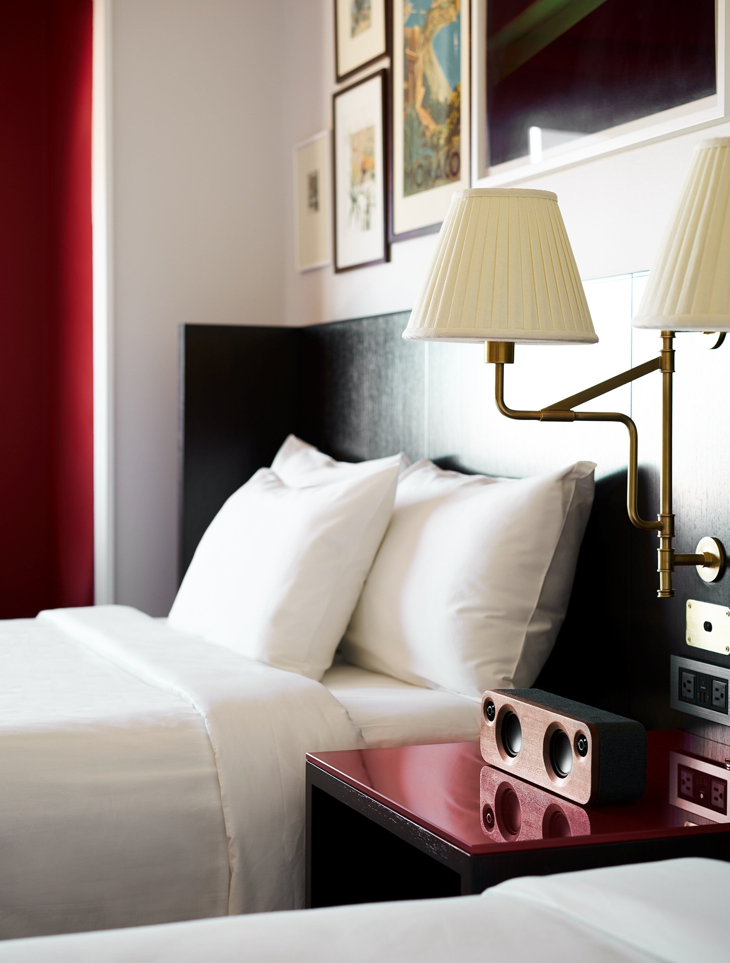 Una habitación de hotel con una cama, dos lámparas de noche, una mesita de noche con lámpara y una pared adornada con cuadros.