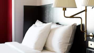 Una habitación de hotel con una cama, dos lámparas de noche, una mesita de noche con lámpara y una pared adornada con cuadros.