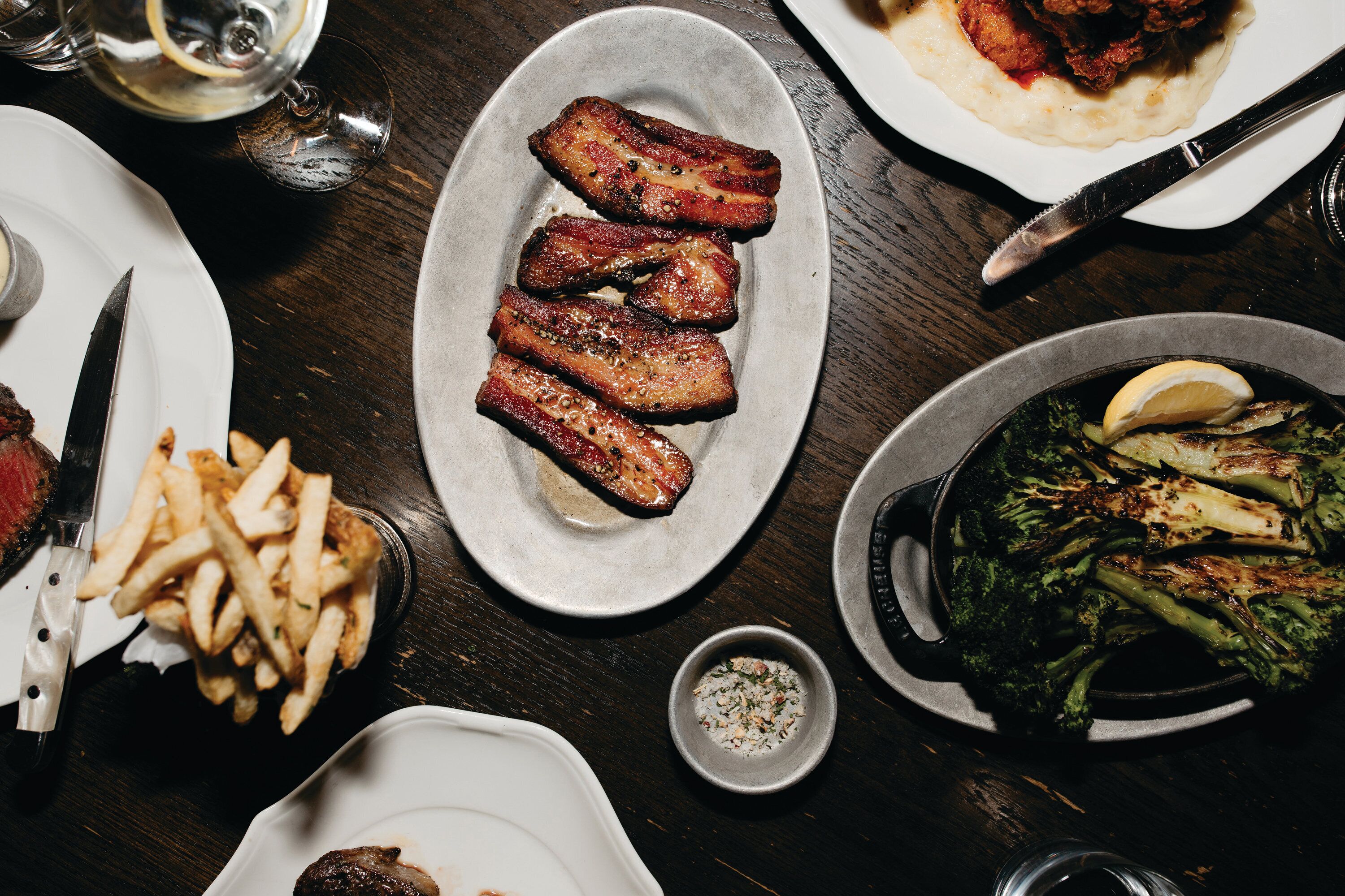 A dining table with various dishes including steak, fries, and roasted vegetables.