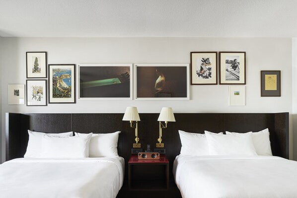 Une chambre d’hôtel avec deux lits, une table de chevet avec des lampes et un mur décoré de tableaux encadrés.