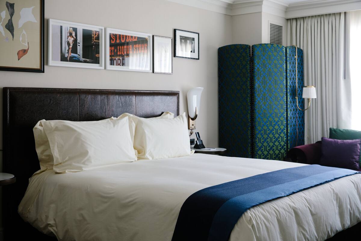 A hotel room with a large bed, a nightstand, a lamp, and a blue patterned partition.