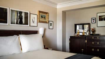 Une chambre d’hôtel avec un grand lit, une commode avec des tiroirs, un miroir et des tableaux encadrés accrochés au mur.