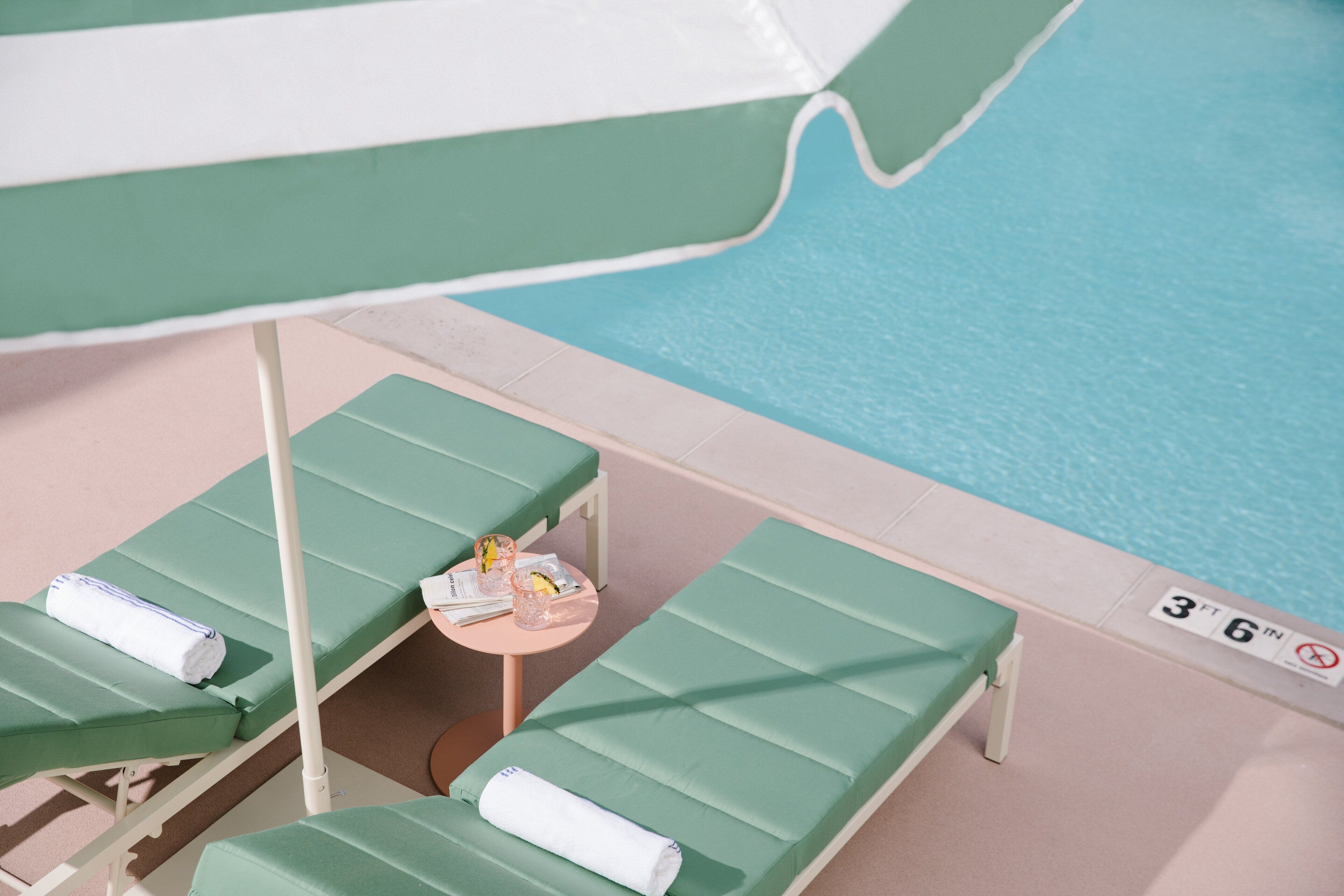 Un espace aménagé au bord de la piscine, avec des chaises longues et une table sur laquelle sont posés une serviette et un verre.