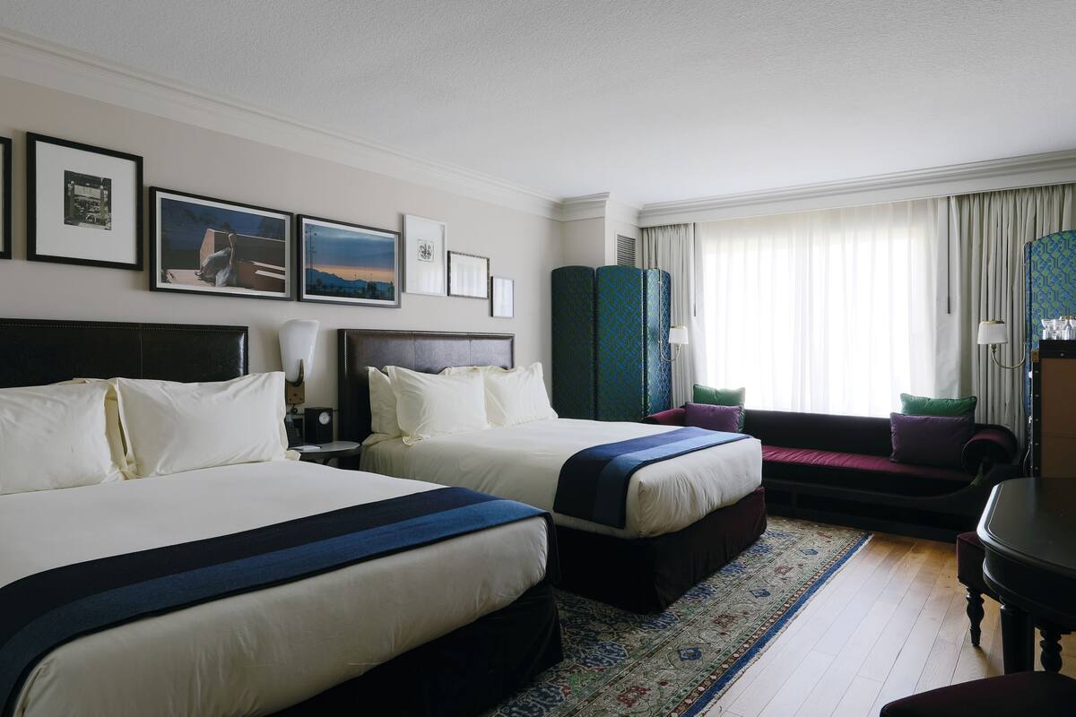 A hotel room with two beds, a sofa, a desk, and a large window with curtains.