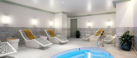 Un área de piscina interior moderna con sillas de descanso y una piscina central.