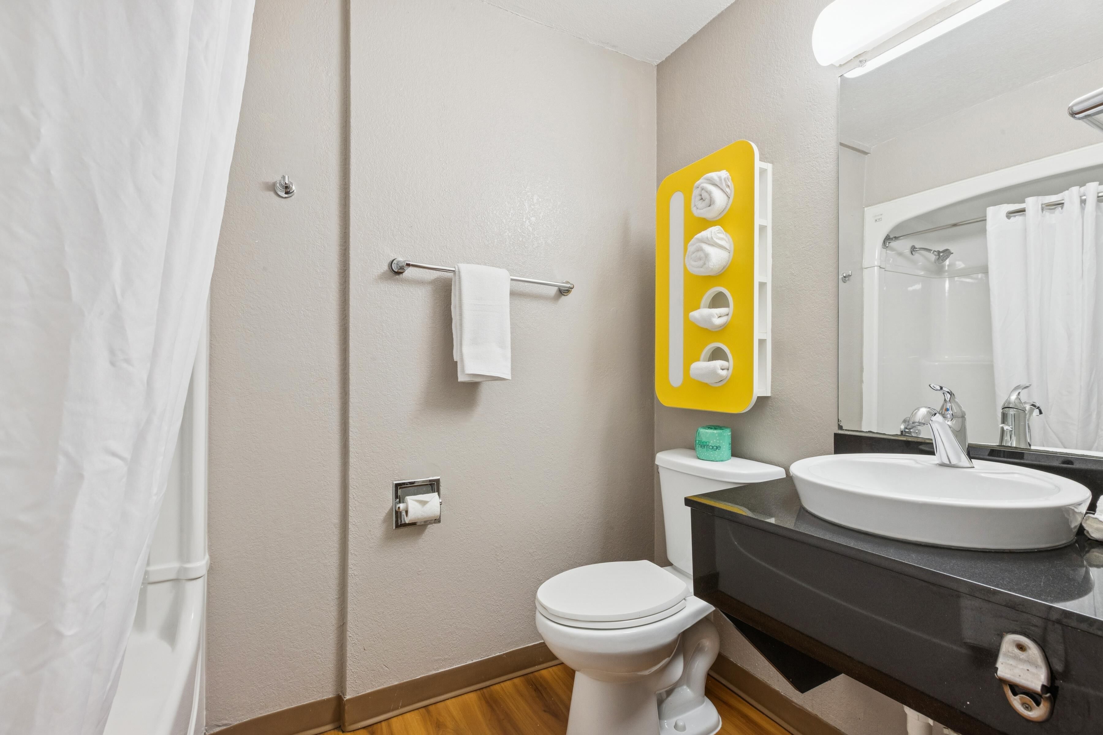 A bathroom with a white toilet, a sink with a mirror above it, and a shower area.
