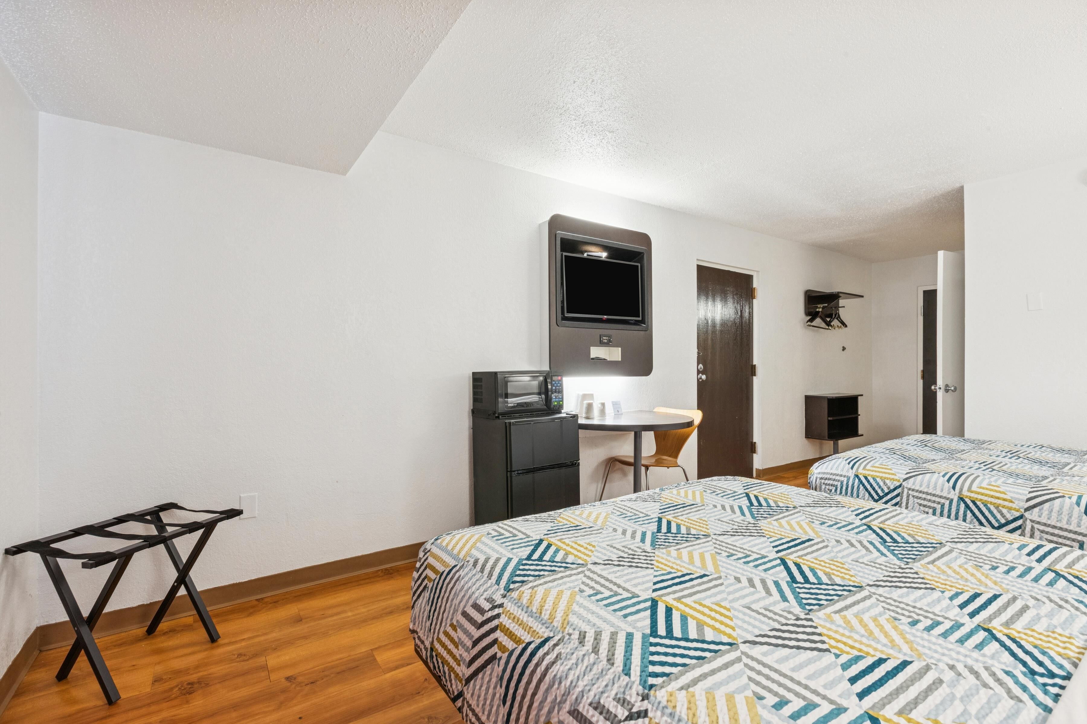 A hotel room with two beds, a desk, a microwave, and a TV.