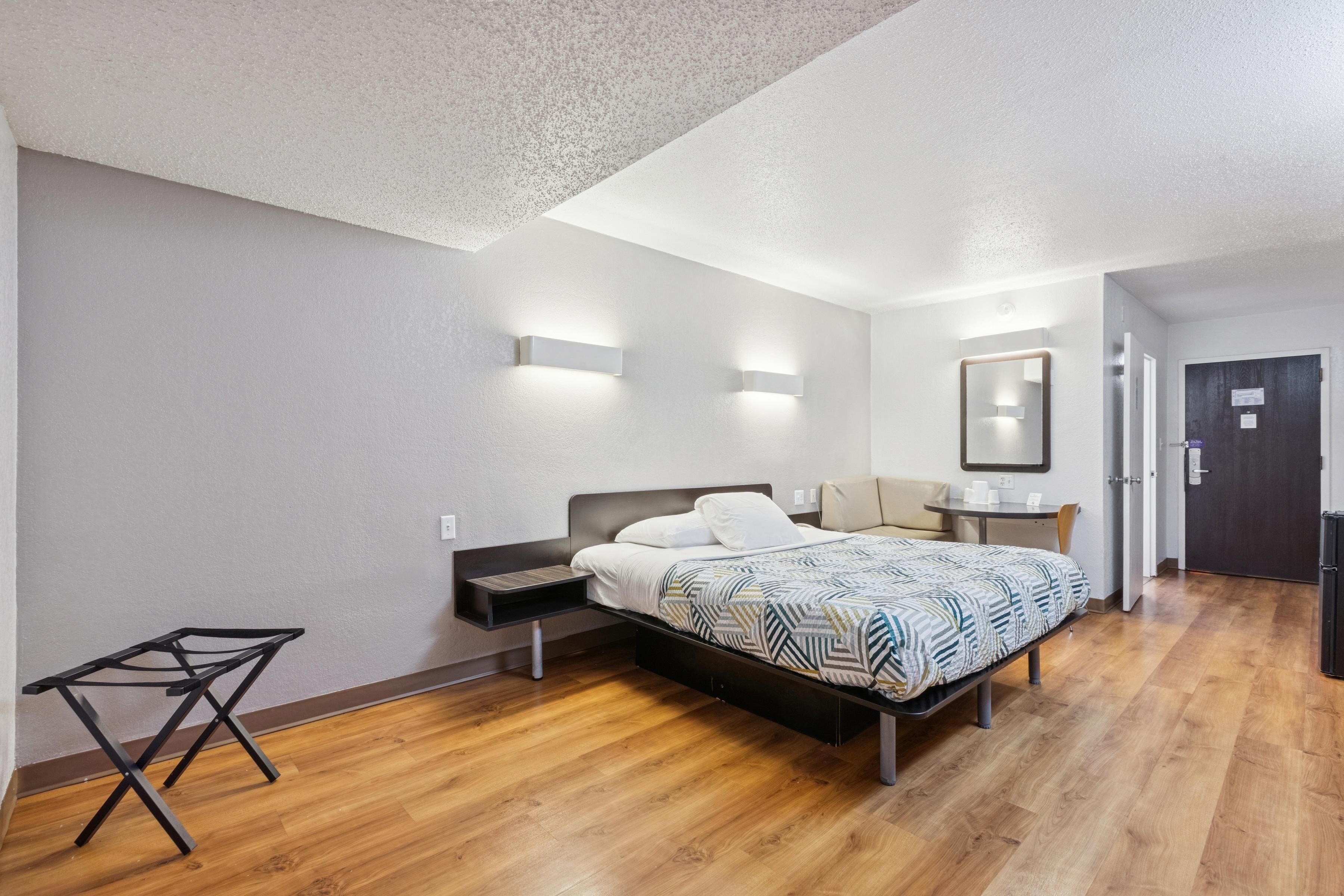 A modern bedroom with a bed, bedside tables, a small desk, and a mirror.