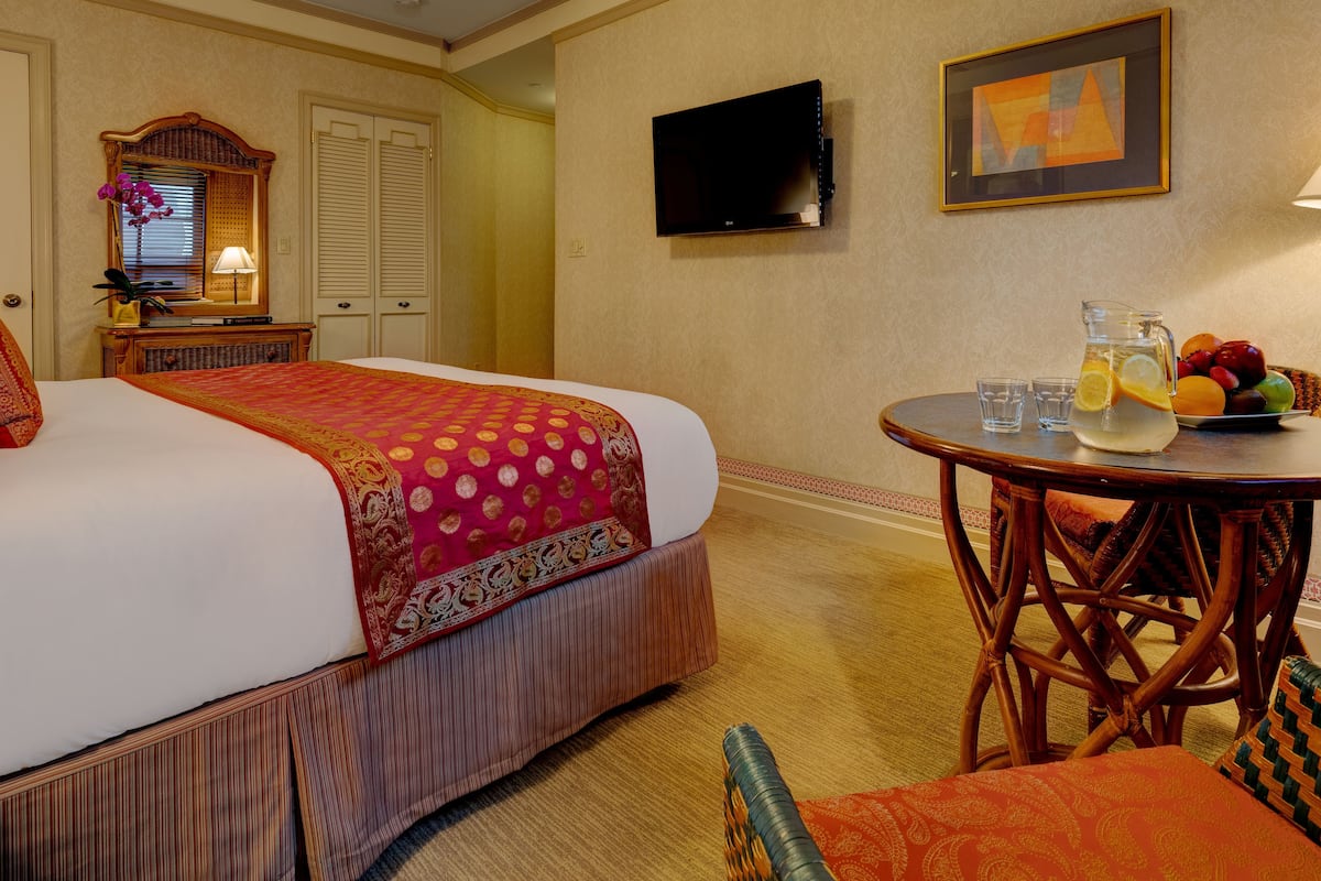 Een hotelkamer met een groot bed, een aan de muur bevestigde televisie, een klein tafeltje met een fruitschaal en glazen, en rieten meubels.