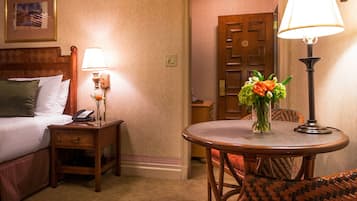 Een hotelkamer met een bed, nachtkastje, lamp en een klein rond tafeltje met een bloemenvaas.
