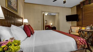 A hotel room with a large bed, a ceiling fan, a television, and a dining area with a table and chairs.