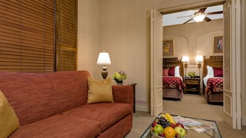 Habitación de hotel con sofá rojo, mesa de centro de vidrio con fruta, lámpara y ventilador de techo.