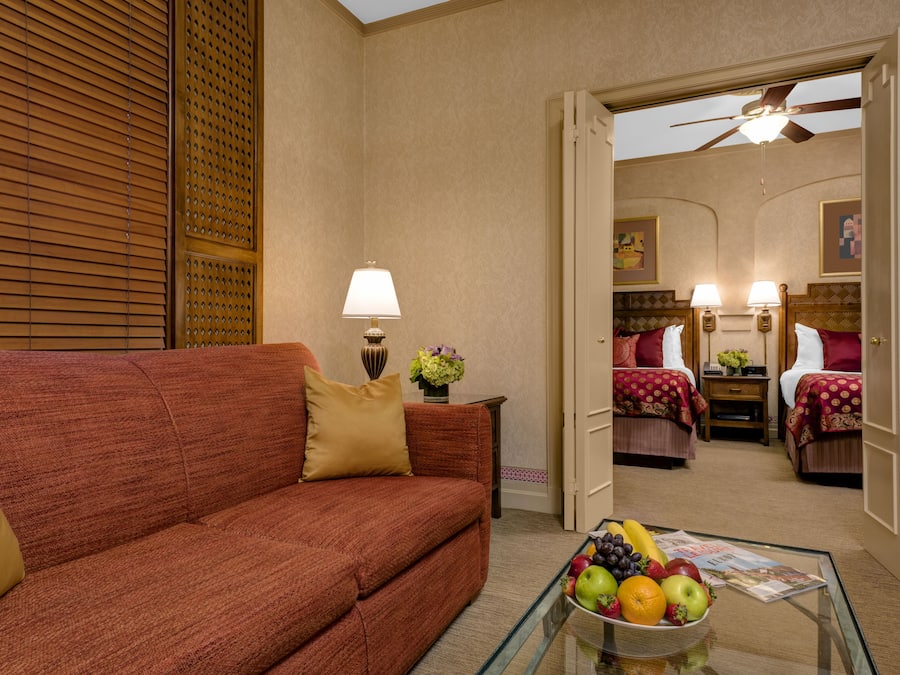 A hotel room with a red sofa, a glass coffee table with fruit, a lamp, and a ceiling fan.