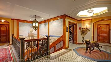 Un vaste hall d’entrée avec un escalier, une fresque représentant un paysage urbain, une statue de chien décorative et un tapis à motifs.