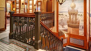Una majestuosa escalera con barandillas ornamentales y un mural con vistas a la ciudad.