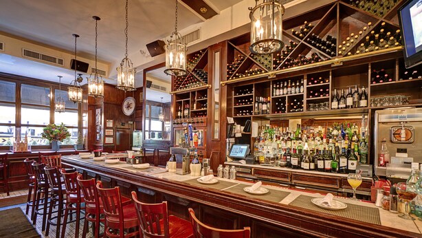 Un bar con sillas de madera, una estantería para vinos y una barra con botellas y copas.
