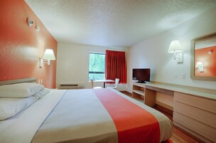 Une chambre d’hôtel avec un lit, un bureau, une télévision et une fenêtre avec des rideaux rouges.