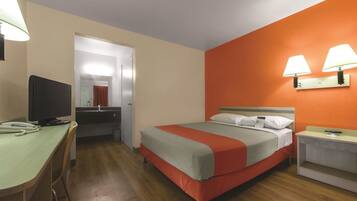 A hotel room with a bed, a desk, a television, and a bathroom visible through an open door.
