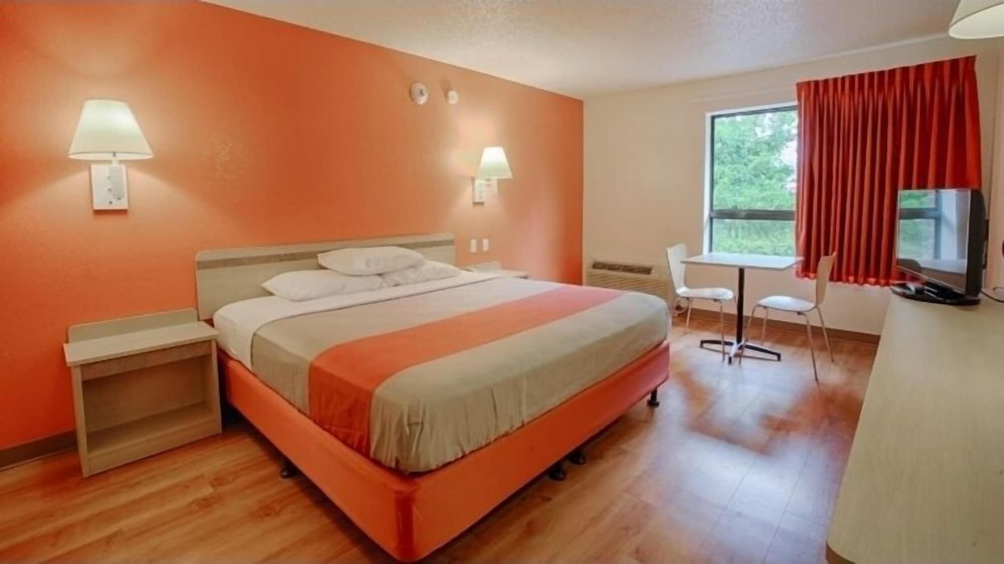 A hotel room with a bed, bedside tables, a desk, a chair, and a television.