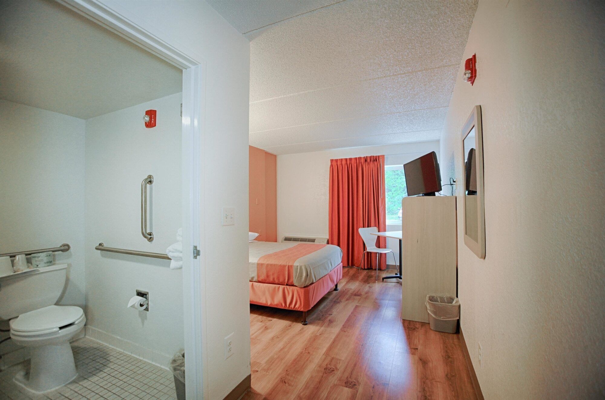 A hotel room with a bathroom, a bed, a desk, a chair, and a television.