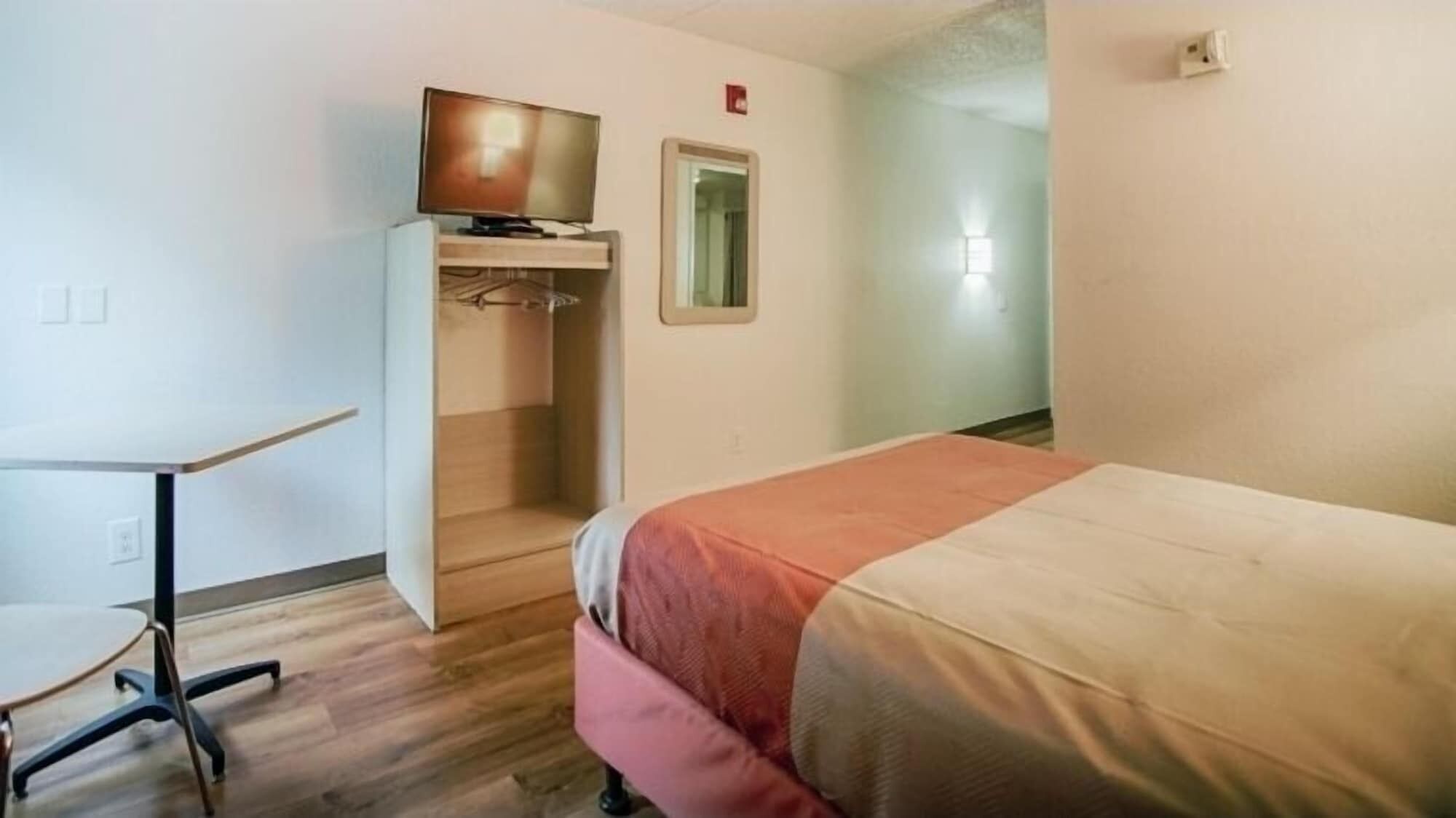 A hotel room with a bed, a desk, and a television on a stand.
