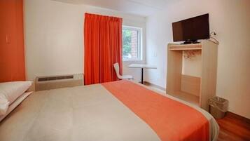A hotel room with a bed, a TV on a stand, a window with curtains, a chair, and a small table.