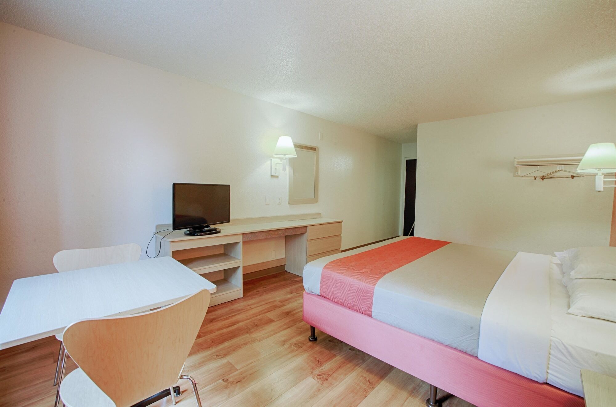 Una habitación de hotel con una cama, un escritorio, una silla, un televisor y un espejo.
