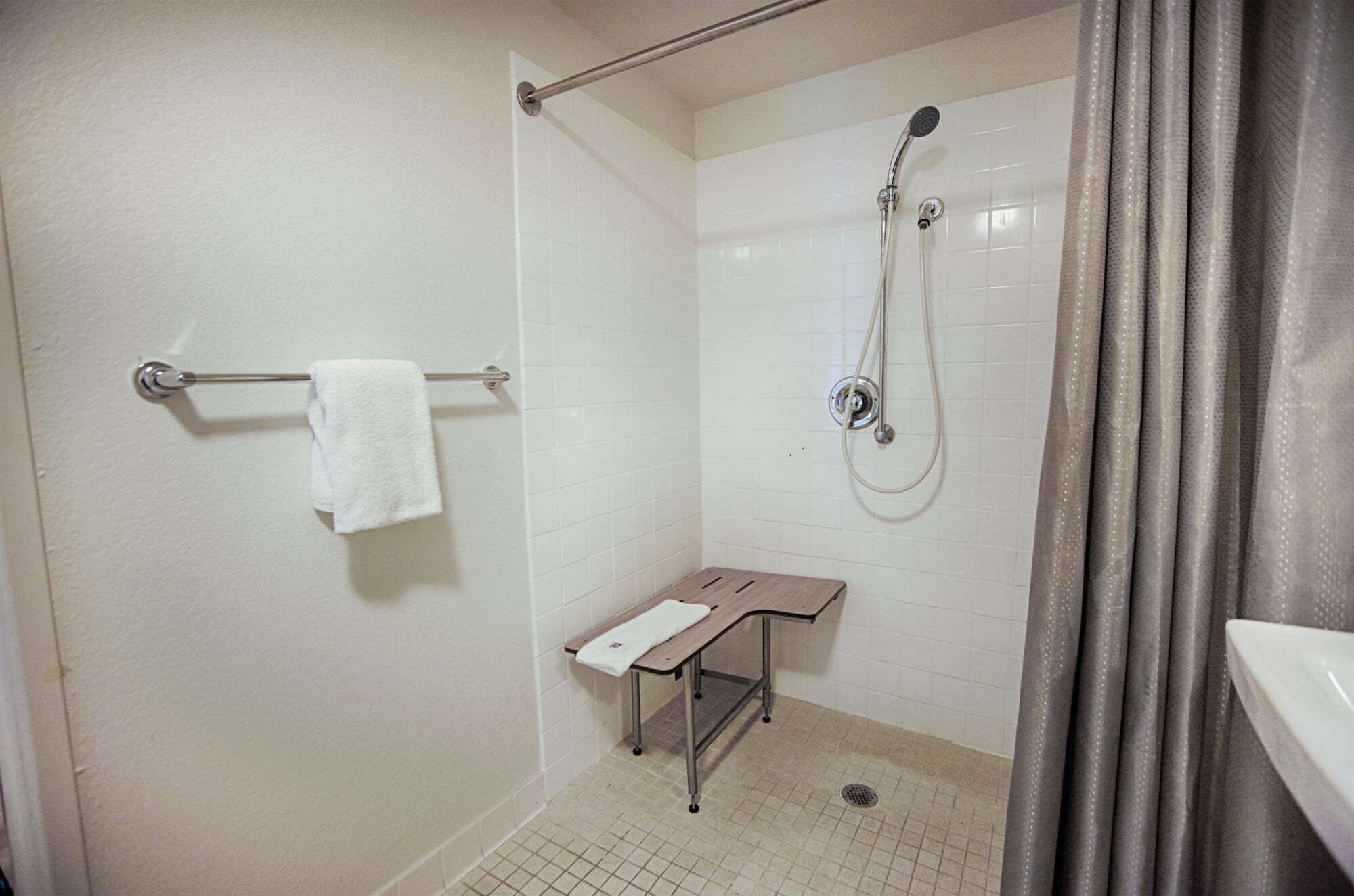 Un baño pequeño y limpio con ducha, perchero y un banco.