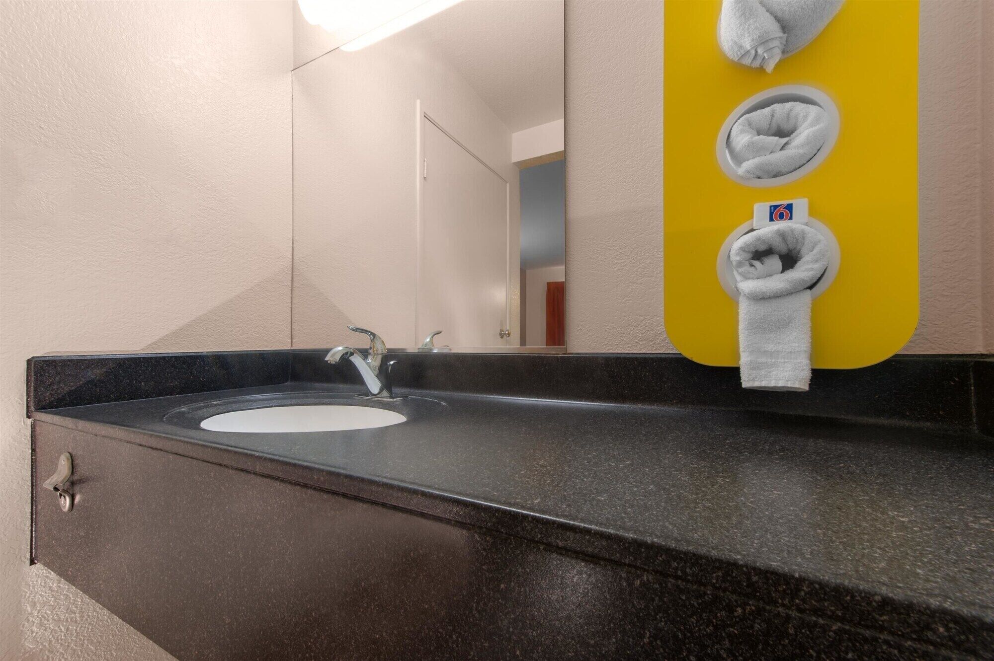 A bathroom with a black granite sink, a mirror, and a yellow towel dispenser with two towels.