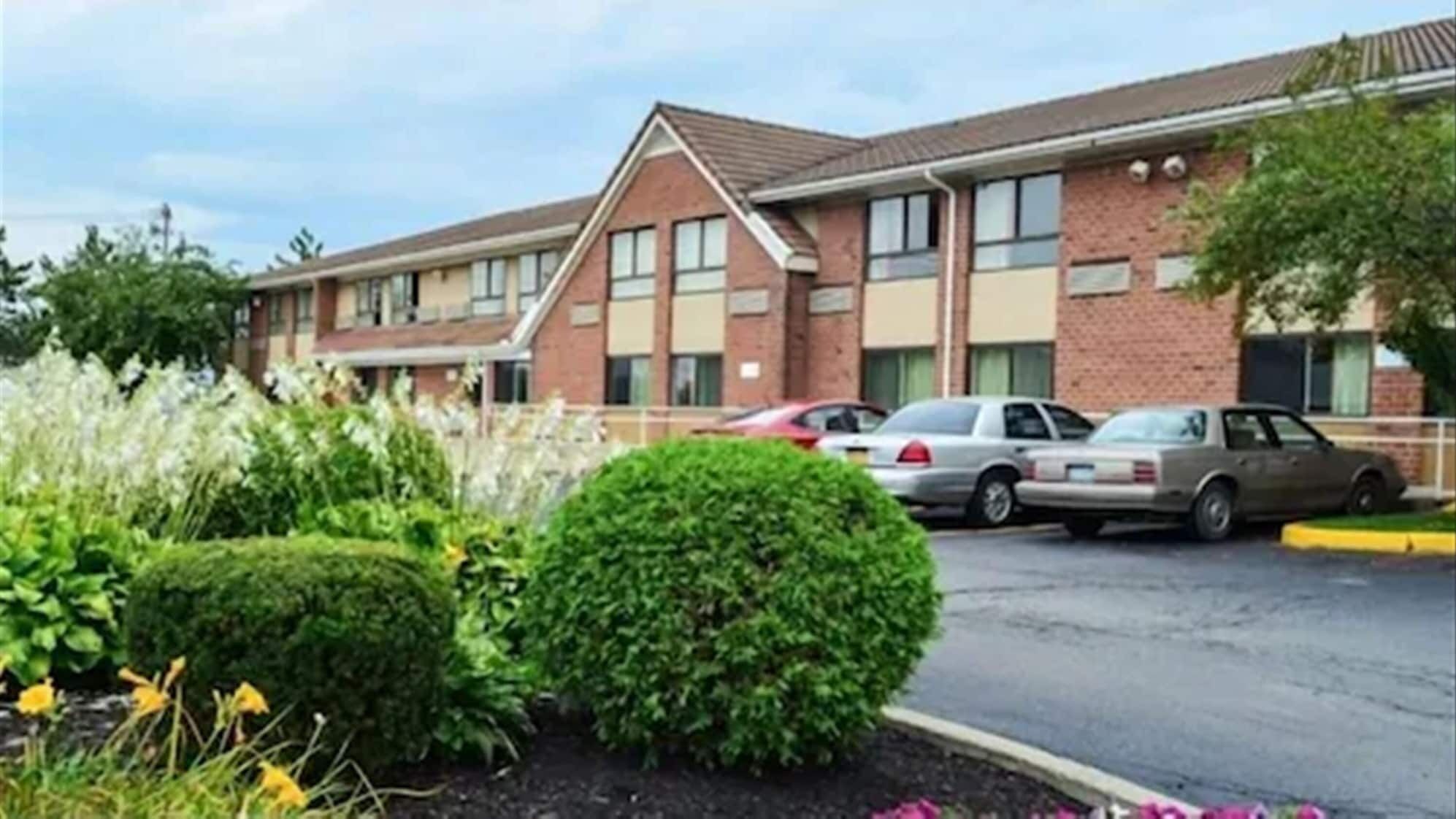 A hotel with a brick facade, multiple windows, and a parking lot with several cars.