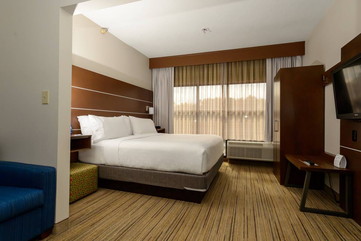 Une chambre d’hôtel avec un grand lit, une télévision, un bureau et une fenêtre avec des rideaux.