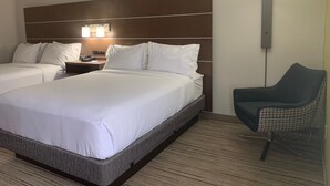 A hotel room with two beds, a nightstand, a lamp, and a chair.
