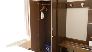 A hotel room with a wardrobe, a bench, and a remote control on the bench.