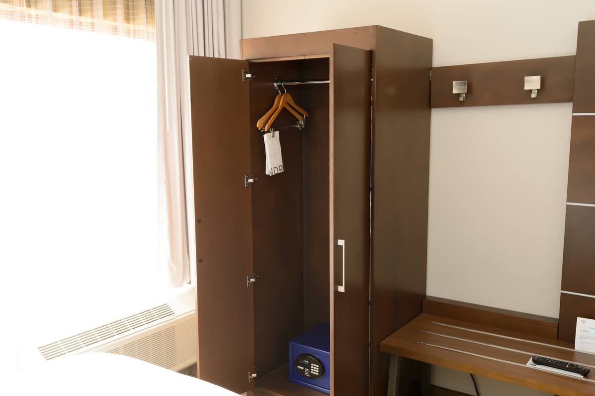 Une chambre d’hôtel avec un placard, un banc et une télécommande posée sur le banc.