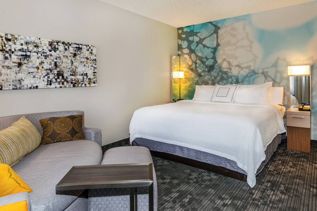 Habitación de hotel con cama, sofá, una mesita y una pared decorada con arte abstracto.