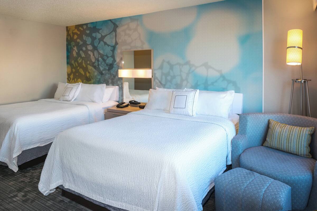 Una habitación de hotel con dos camas, una mesita de noche, una lámpara y una silla.