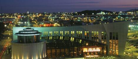 A modern building with a circular tower and a curved facade, surrounded by a parking lot and a cityscape at dusk.